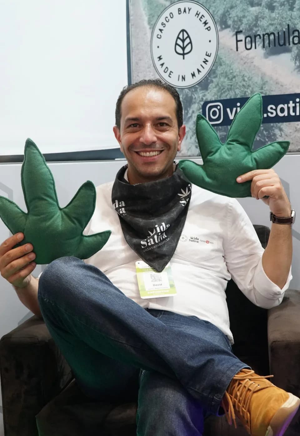 Sócio da Vida Sativa em um estande de feira, sorrindo e segurando duas almofadas em formato de folha de cannabis